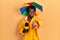 Young african american journalist man wearing yellow raincoat and umbrella cap pointing with finger to the camera and to you,