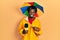 Young african american journalist man wearing yellow raincoat and umbrella cap smiling happy pointing with hand and finger