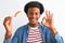 Young african american man eating nigiri using chopsticks over isolated white background doing ok sign with fingers, excellent