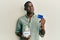 Young african american man holding credit card and jar with dollars smiling looking to the side and staring away thinking