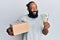 Young african american man holding delivery box and usa dollars banknotes smiling looking to the side and staring away thinking