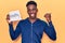 Young african american man holding healthy hashtag paper pointing thumb up to the side smiling happy with open mouth