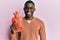 Young african american man holding heat water bag looking positive and happy standing and smiling with a confident smile showing