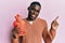 Young african american man holding heat water bag smiling happy pointing with hand and finger to the side