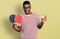 Young african american man holding red ping pong rackets and ball clueless and confused expression
