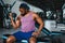 Young African American man sitting and lifting a dumbbell close to the rack at gym. Male weight training person doing a