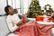 Young african american man sitting on the sofa drinking coffee by christmas tree crazy and mad shouting and yelling with