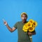 Young African American man standing with bouquet of sunflowers pointing finger sideways up with shock excitement facial