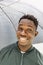 Young African American man under black umbrella in rain, smiling. Fall or spring weather