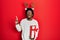 Young african american man wearing deer christmas hat holding gift amazed and surprised looking up and pointing with fingers and