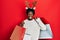 Young african american man wearing deer christmas hat holding shopping bags winking looking at the camera with sexy expression,