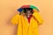 Young african american man wearing yellow raincoat smiling pulling ears with fingers, funny gesture