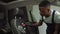 A young African-American man in work clothes works at a car wash, brushes the seat of an expensive car, applies