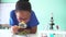 Young African American mixed kid using a magnifying glass on a green plant in chemistry and biology classroom lab