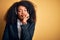 Young african american operator woman with afro hair wearing headset over yellow background thinking looking tired and bored with