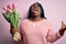 Young african american plus size woman with braids holding bouquet of pink tulips flower crazy and mad shouting and yelling with