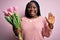 Young african american plus size woman with braids holding bouquet of pink tulips flower Waiving saying hello happy and smiling,