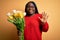 Young african american plus size woman with braids holding bouquet of yellow tulips flower Waiving saying hello happy and smiling,
