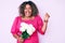 Young african american plus size woman holding flowers screaming proud, celebrating victory and success very excited with raised