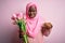 Young african american plus size woman wearing muslim hijab holding bouquet of pink tulips Pointing down looking sad and upset,