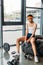 young african american sportswoman in headband and wristbands sitting on training tire with jump rope and bottle of water