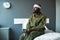 Young African American stressed soldier with bandaged head sitting on bed