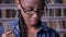 Young african american student in glasses reading book and smiling at camera, bookshelves in library background, happy