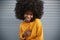 Young African American woman with afro against grey wall, raising shoulder, smiling to camera, close up
