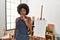 Young african american woman with afro hair at art studio asking to be quiet with finger on lips