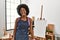 Young african american woman with afro hair at art studio sticking tongue out happy with funny expression