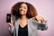 Young african american woman with afro hair holding cracked and broken smartphone screen with surprise face pointing finger to