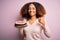 Young african american woman with afro hair holding delicious birthday cake happy with big smile doing ok sign, thumb up with