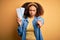 Young african american woman with afro hair holding plane boarding pass for a holiday trip pointing with finger to the camera and