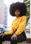 Young African American woman with afro hair and sitting on a chair in the street looking to camera, vertical