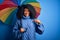 Young african american woman with afro hair under colorful umbrella for winter weather rain with surprise face pointing finger to