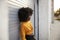 Young African American woman with afro leaning in the street against grey security shutters, side view