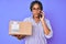 Young african american woman with braids holding delivery box calling assistance relaxed with serious expression on face