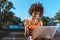 young african-american woman in bright sports bra sitting at sport court with laptop