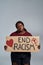 Young african american woman in casual clothes holding End Racism banner in front of her, posing isolated over gray