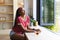 A young African American woman gazes out a window, a cup of tea before her, with copy space