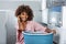 Young African American woman holding a basket of clothes to be washed in a automatic laundry