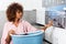 Young African American woman holding a basket of clothes to be washed in a automatic laundry