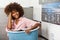 Young African American woman holding a basket of clothes to be washed in a automatic laundry