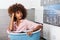 Young African American woman holding a basket of clothes to be washed in a automatic laundry