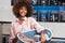 Young African American woman holding a basket of clothes to be washed in a automatic laundry