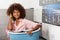 Young African American woman holding a basket of clothes to be washed in a automatic laundry