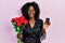 Young african american woman holding bouquet of flowers and engagement ring smiling and laughing hard out loud because funny crazy