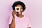 Young african american woman holding bread loaf with heart shape sticking tongue out happy with funny expression