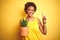 Young african american woman holding cactus pot over isolated yellow background surprised with an idea or question pointing finger