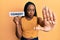 Young african american woman holding comedy word paper with open hand doing stop sign with serious and confident expression,